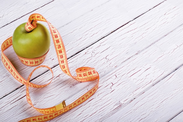 Free photo green apple and orange tape-measure lie on white wooden floor