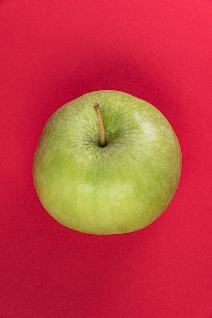 Зеленое яблоко на красном фоне