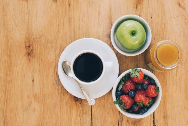Green apple; sweet jam; berries and black coffee cup on wooden textured backdrop