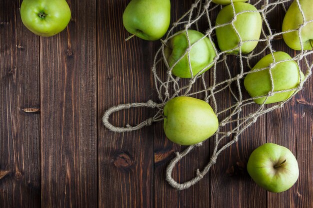 Green apples in a net bag and around on a wooden background. top view. space for text