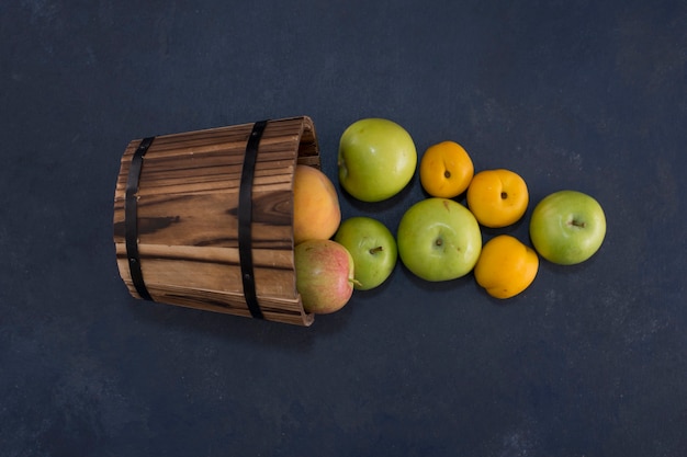 Free photo green apples and oranges out of a wooden bucket in the middle.