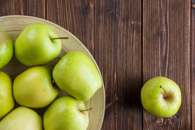 зеленые яблоки в тарелку и вокруг вид сверху на деревянном фоне пространства для текста