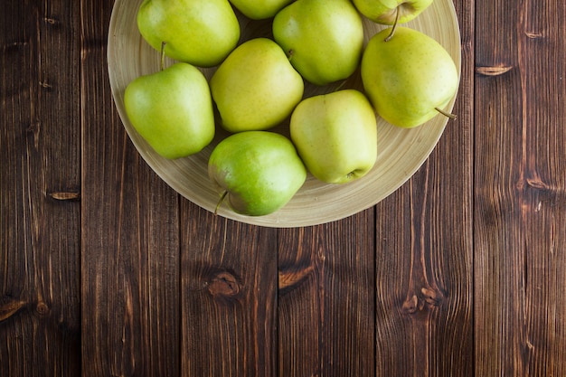 Free photo green apples in a plate on a wooden background. top view. space for text