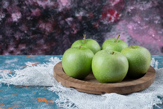 Green apples on wooden platter on blue.