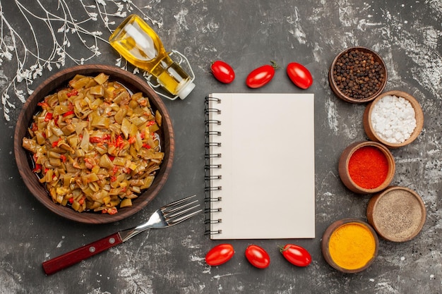 green beans with tomatoes the appetizing green beans and tomatoes next to the fork bottle of oil bowls of colorful spices tomatoes and white notebook on the table