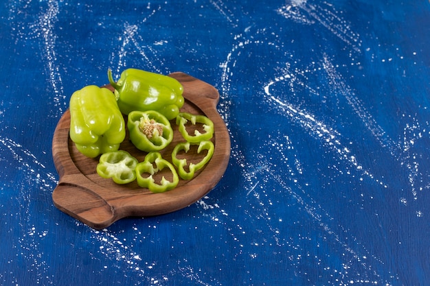 Free photo green bell peppers and rings on wooden board on marble surface