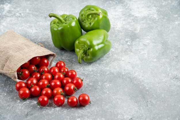 Green bell peppers with cherry tomatoes inside rustic bag on marble table.