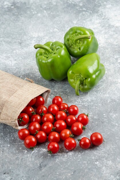 Green bell peppers with cherry tomatoes inside rustic bag on marble table.