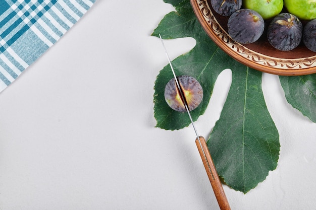 Зеленый и черный инжир на керамической тарелке с ножом и листом. Фото высокого качества