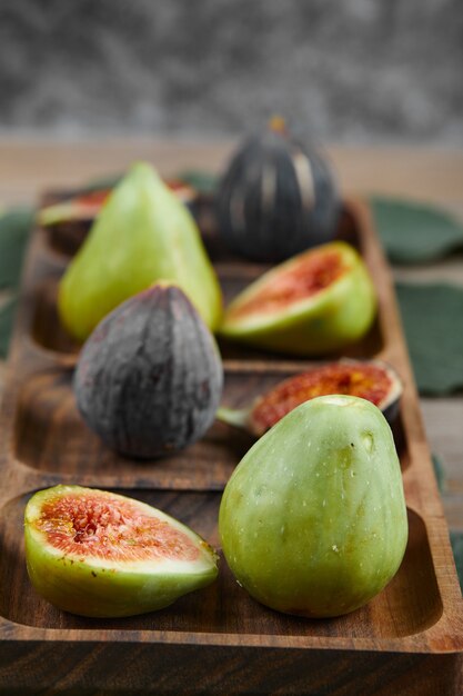 Green and black figs on a wooden platter with leaves and tablecloth, close up. High quality photo