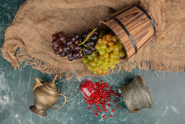 Green and black grapes and pomegranate seeds on marble surface.