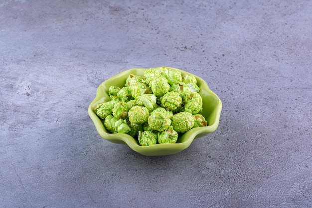 Foto gratuita ciotola verde che tiene un mucchio modesto di popcorn ricoperto di caramelle sulla superficie di marmo