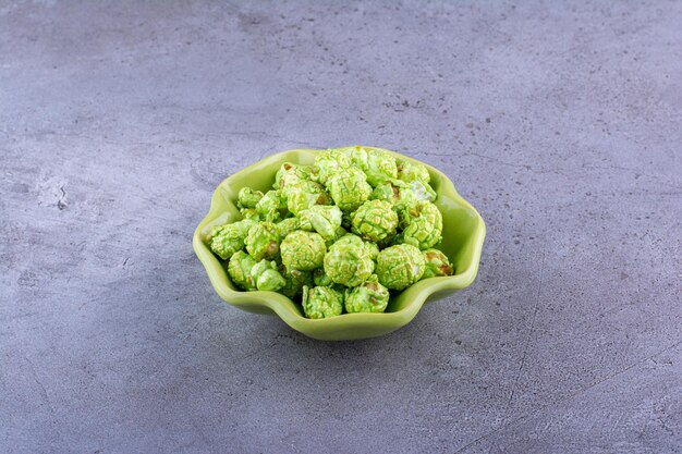 Green bowl holding a modest heap of candy coated popcorn on marble surface