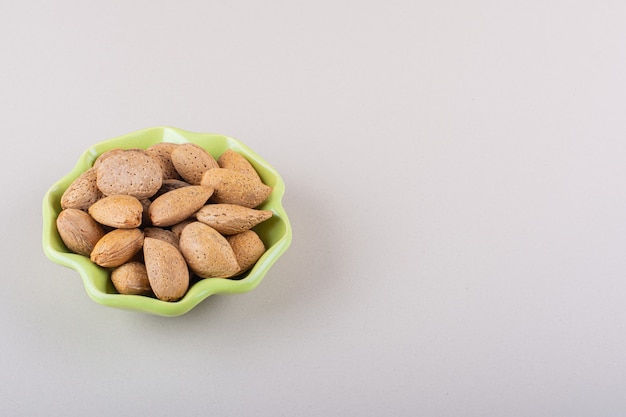 Free photo green bowl of shelled organic almonds on white background. high quality photo