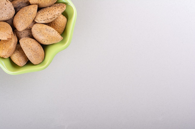 Green bowl of shelled organic almonds on white background. High quality photo