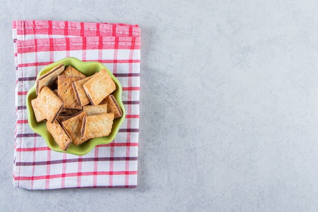 Green bowl of tasty crunchy crackers on stone.