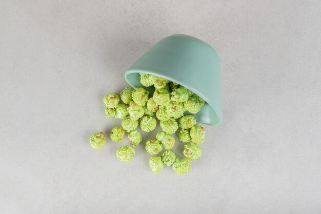 Foto gratuita popcorn verdi e canditi sparsi da una piccola ciotola sul tavolo di marmo.