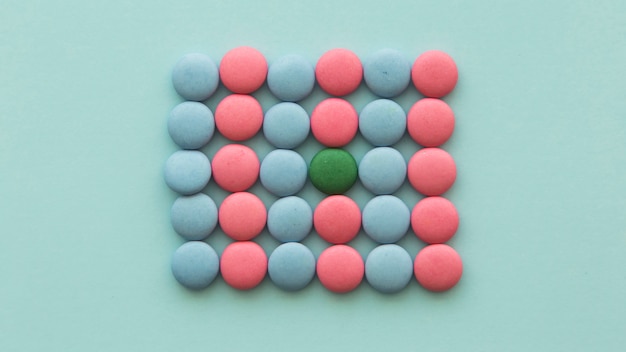 Green candy arranged in the pink and blue candies on colored background