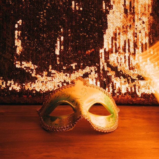 Зеленая карнавальная маска на деревянном столе с блестками золотого блеска