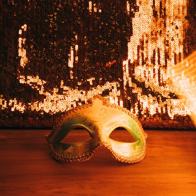 Green carnival mask on wooden desk with golden glitter sequins