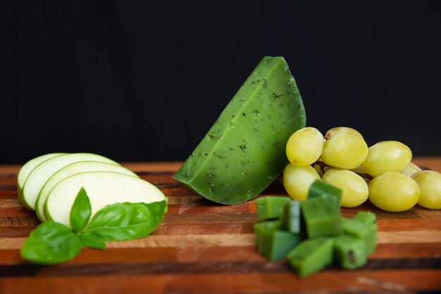 Green cheese, sliced apple and grapes laying on wooden board