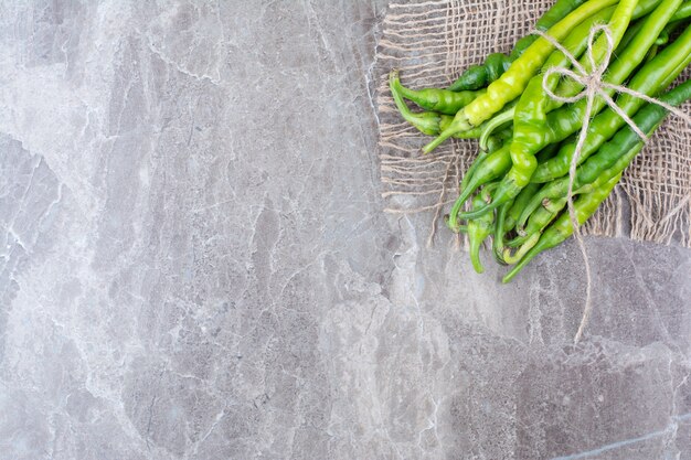 Green chili peppers tied with rope on burlap.