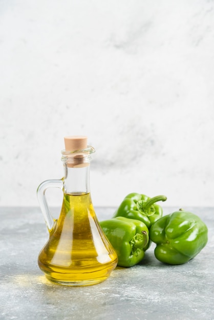 Green chili peppers with a bottle of extra virgin olive oil on marble table.