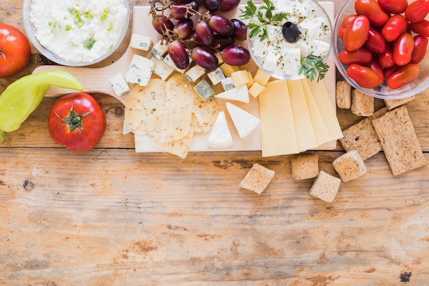 Green chilies pepper, tomatoes, grapes, crisp bread and cheese cubes on desk