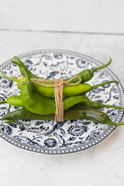 Green chilies tied with string on ceramic plate against textured backdrop