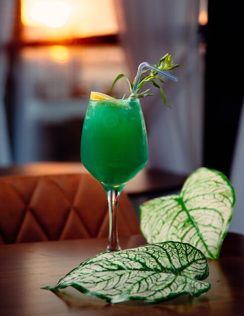 Green cocktail with lemon slice and mint leaves.
