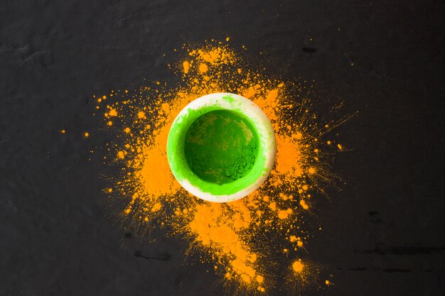 Green color powder in bowl with yellow powder splatter on black background