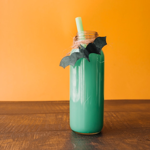 Green colour drink in bottle with handmade bat on orange background