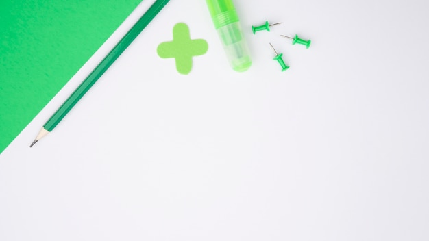 Free photo green craft paper; pencil; glue and push pin over white surface