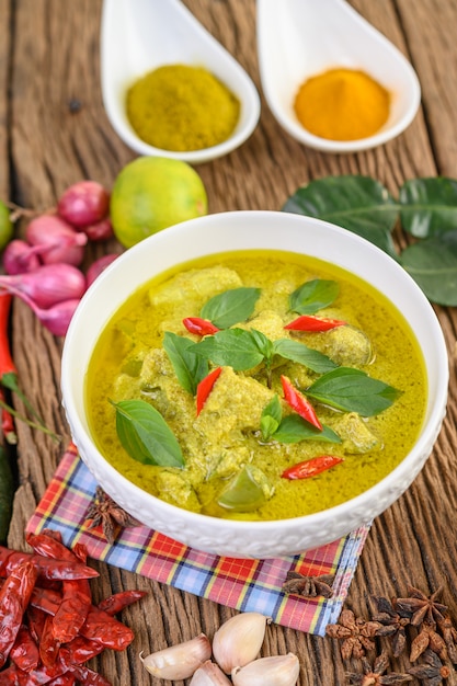 Green curry in a bowl and spices on wooden table.