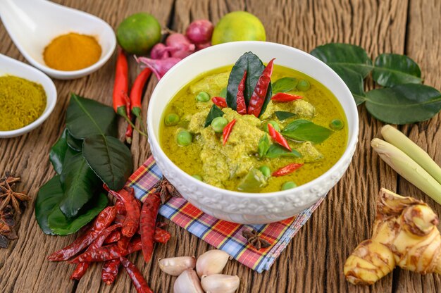 Green curry in a bowl and spices on wooden table.