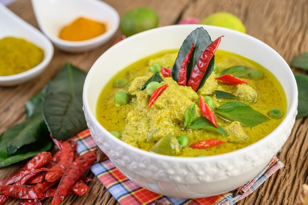 Green curry in a bowl and spices on wooden table.