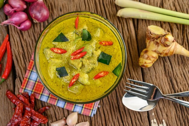 Green curry in a bowl with fork and spoon on wooden table.