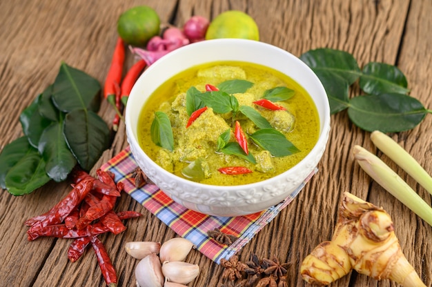 Green curry in a bowl with lime, red onion, lemon grass, garlic and kaffir lime leaves