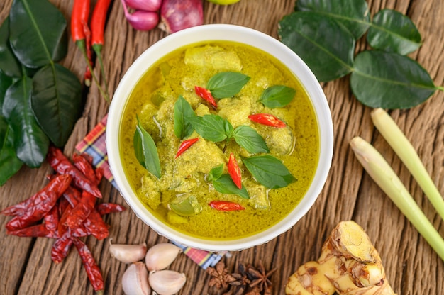 Green curry in a bowl with lime, red onion, lemon grass, garlic and kaffir lime leaves