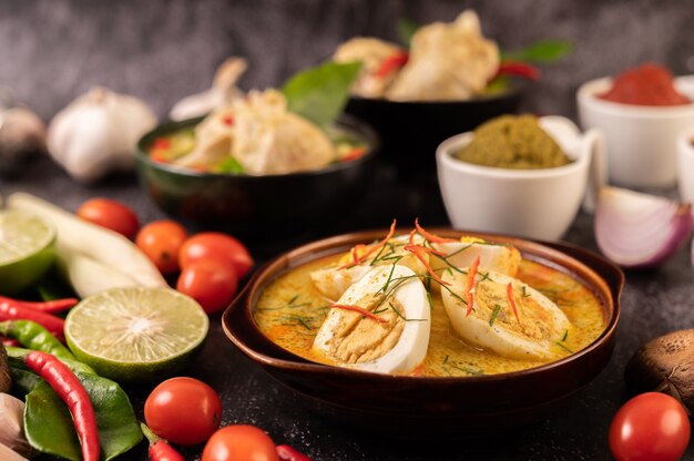 Green curry with eggs in black cups, with lemon, lemongrass, chili, and tomatoes.