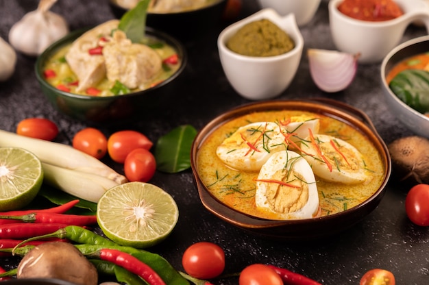 Green curry with eggs in black cups, with lemon, lemongrass, chili, and tomatoes.