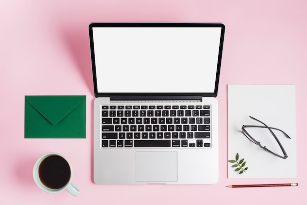 Green envelope; tea cup; laptop; eyeglasses on paper and pencil on pink backdrop