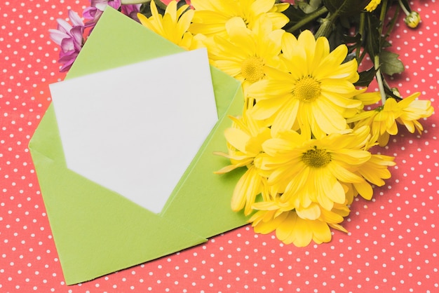 Free photo green envelope with piece of paper and yellow daisies