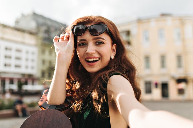 Green eyed lady putting off sunglasses and taking selfie