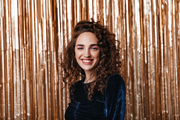 Green eyed lady in velvet blouse smiling on gold background