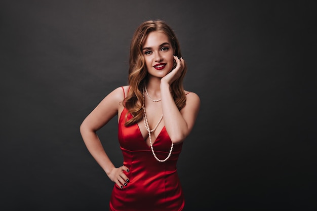 Green eyed lady with red lips looks into camera on black background Woman with gorgeous makeup dressed in silk dress smiling on isolated backdrop