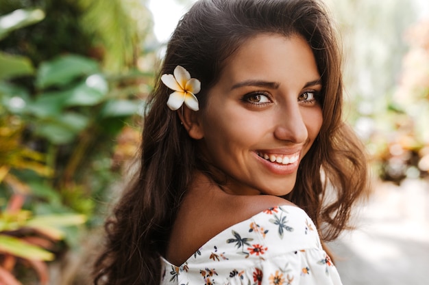 Green-eyed lady with tanned skin smiles sweetly against wall of palm trees