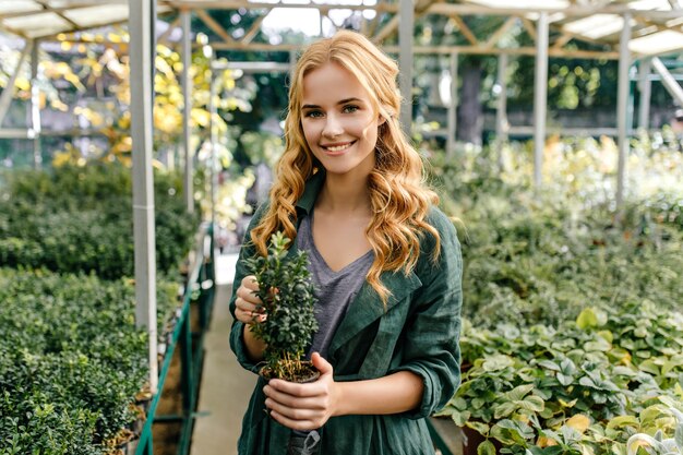 Green-eyed red-haired girl loves nature. Cute model posing with smile, holding plant in her hands.