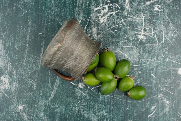 Green feijoa fruits falling out of the vase on marble surface.