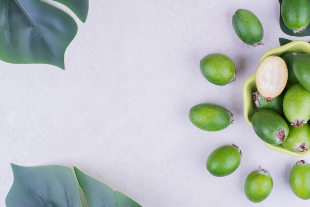 Green feijoas in a cup with leaves around.